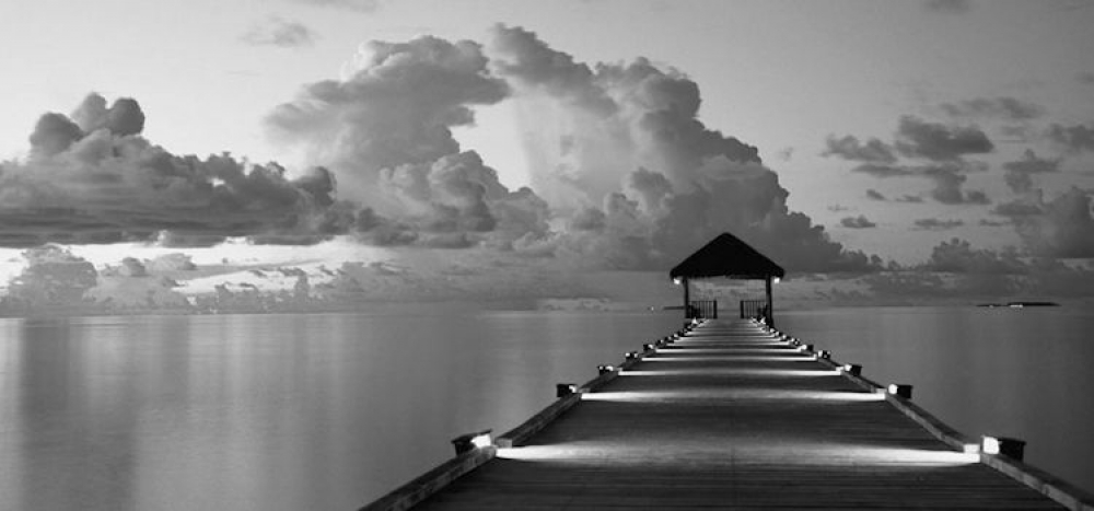 Illuminated dock leads out to distance on still waters with cloudy skies.